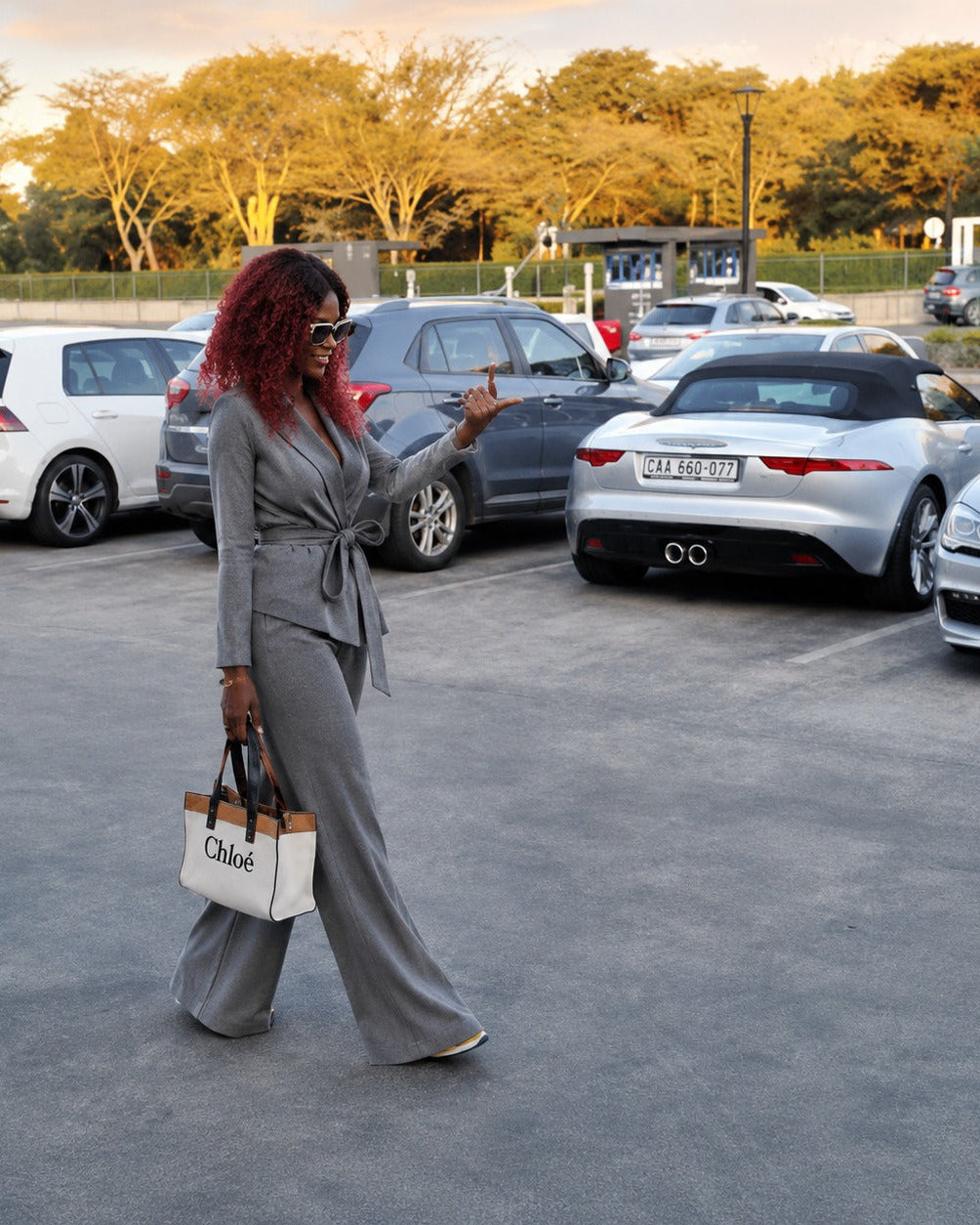 Woman in a gray suit standing in a parking lot with cars and trees in the background
